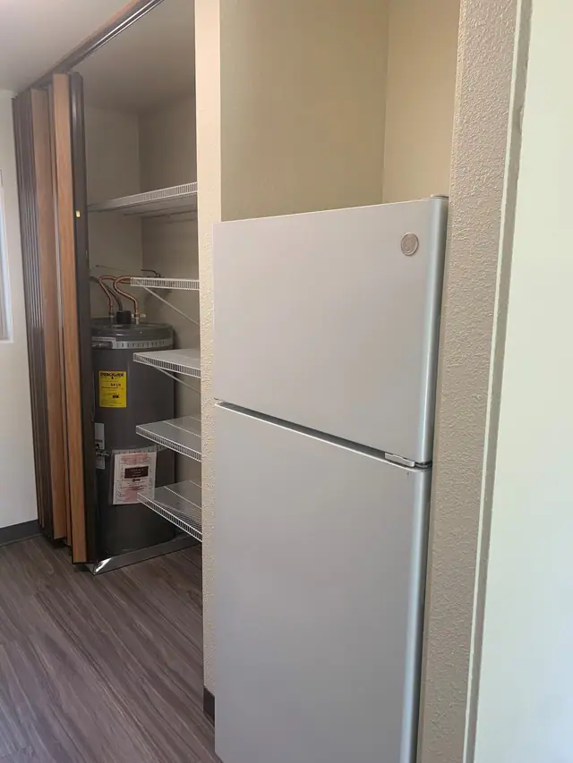 Refrigerator beside a shelved closet with the water heater