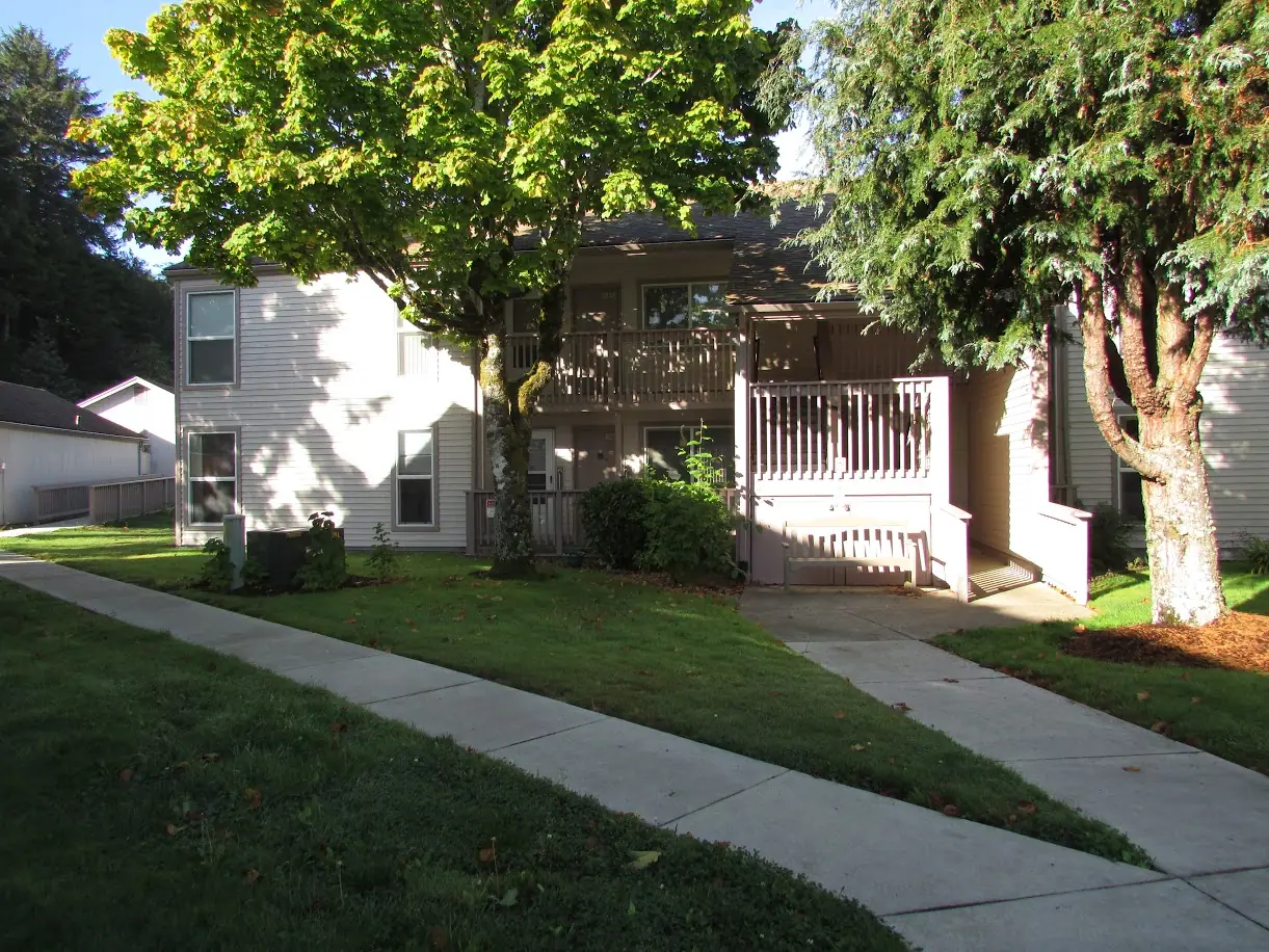Two-story building with a covered entry, a bench and shade trees