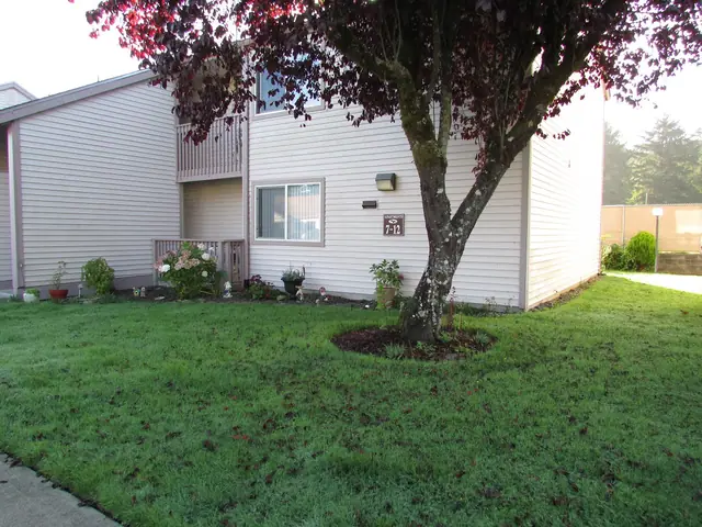 Building for apartments 7 to 12 with a lawn, a tree and flower beds